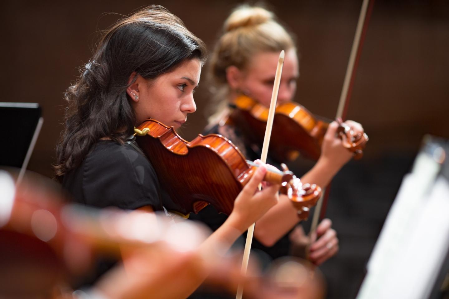 A student plays the violin in-focus with the rest of the orchestra